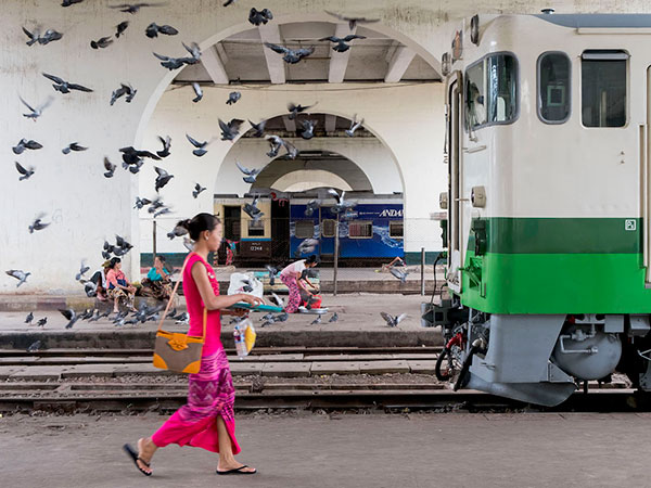 ヤンゴン中央駅の日中の様子。陸橋の下、日本の車両と列車に乗る女性。